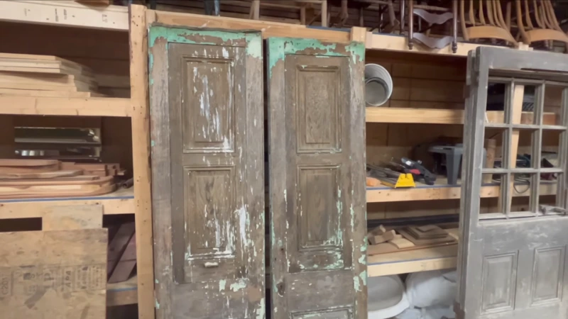 Customer examining vintage architectural elements and antique doors in organized salvage warehouse with price tags visible