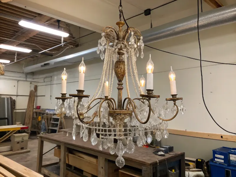 Restored antique chandelier hanging in workshop with exposed new wiring and modern electrical components